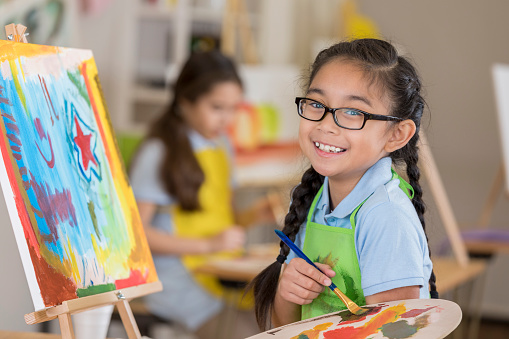 Beautiful Filipino elementary age art student smiles while working on a painting in art class.