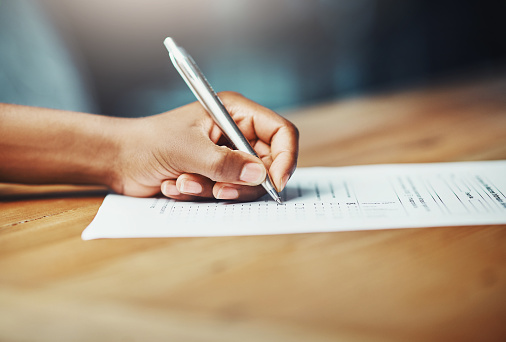 Cropped shot of a woman filling in some paperwork at a desk